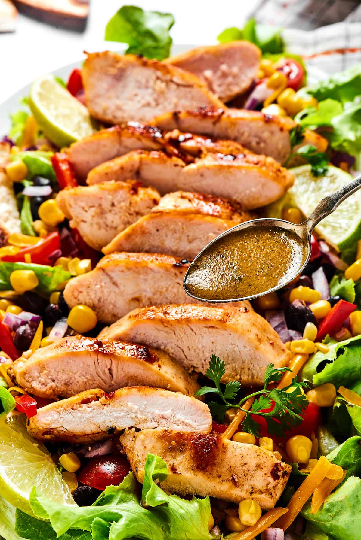 With ingredients like black beans, corn, bell pepper, and tomatoes, this Grilled Chicken Southwest Salad is bursting with flavor. A spoon of vinaigrette being drizzled over southwest salad