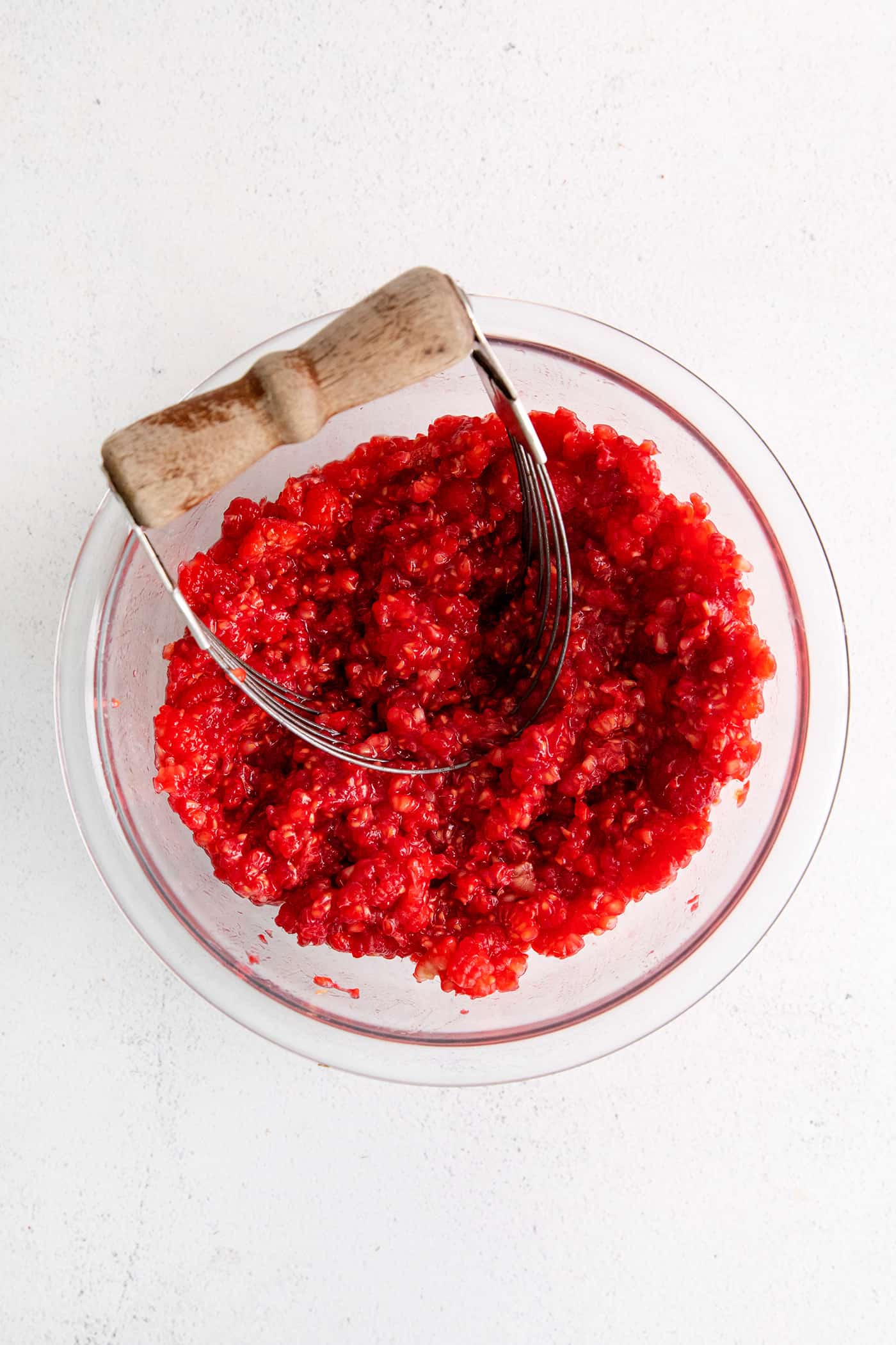 This Raspberry Blackberry Freezer Jam comes together in less than an hour, with just 4 ingredients. No cooking or canning is required! A potato masher mashing raspberries