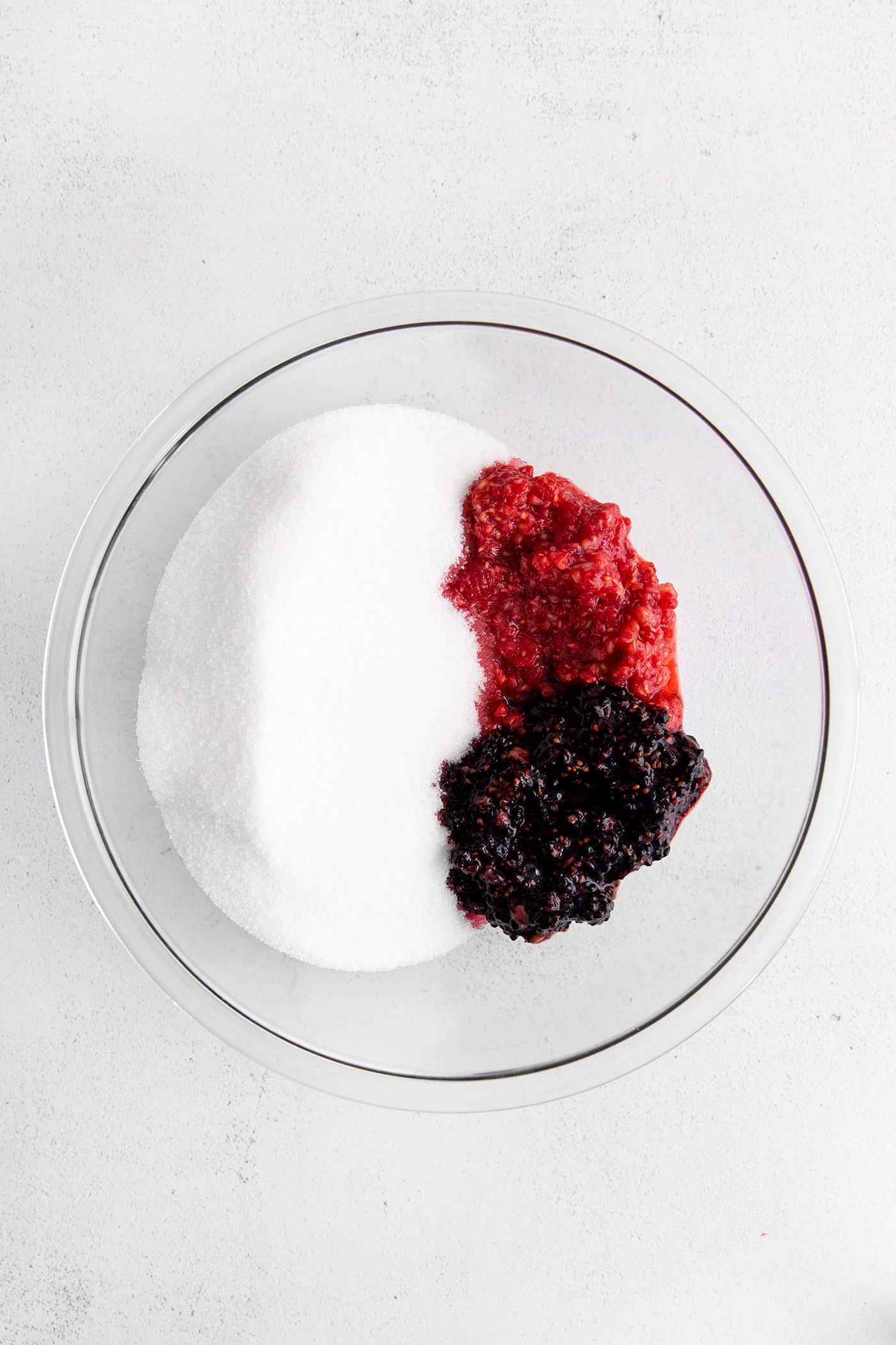This Raspberry Blackberry Freezer Jam comes together in less than an hour, with just 4 ingredients. No cooking or canning is required! Mashed raspberries and blackberries in a bowl with sugar