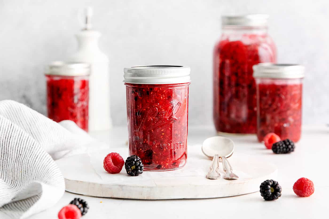 This Raspberry Blackberry Freezer Jam comes together in less than an hour, with just 4 ingredients. No cooking or canning is required! A jar of raspberry freezer jam on a white plate