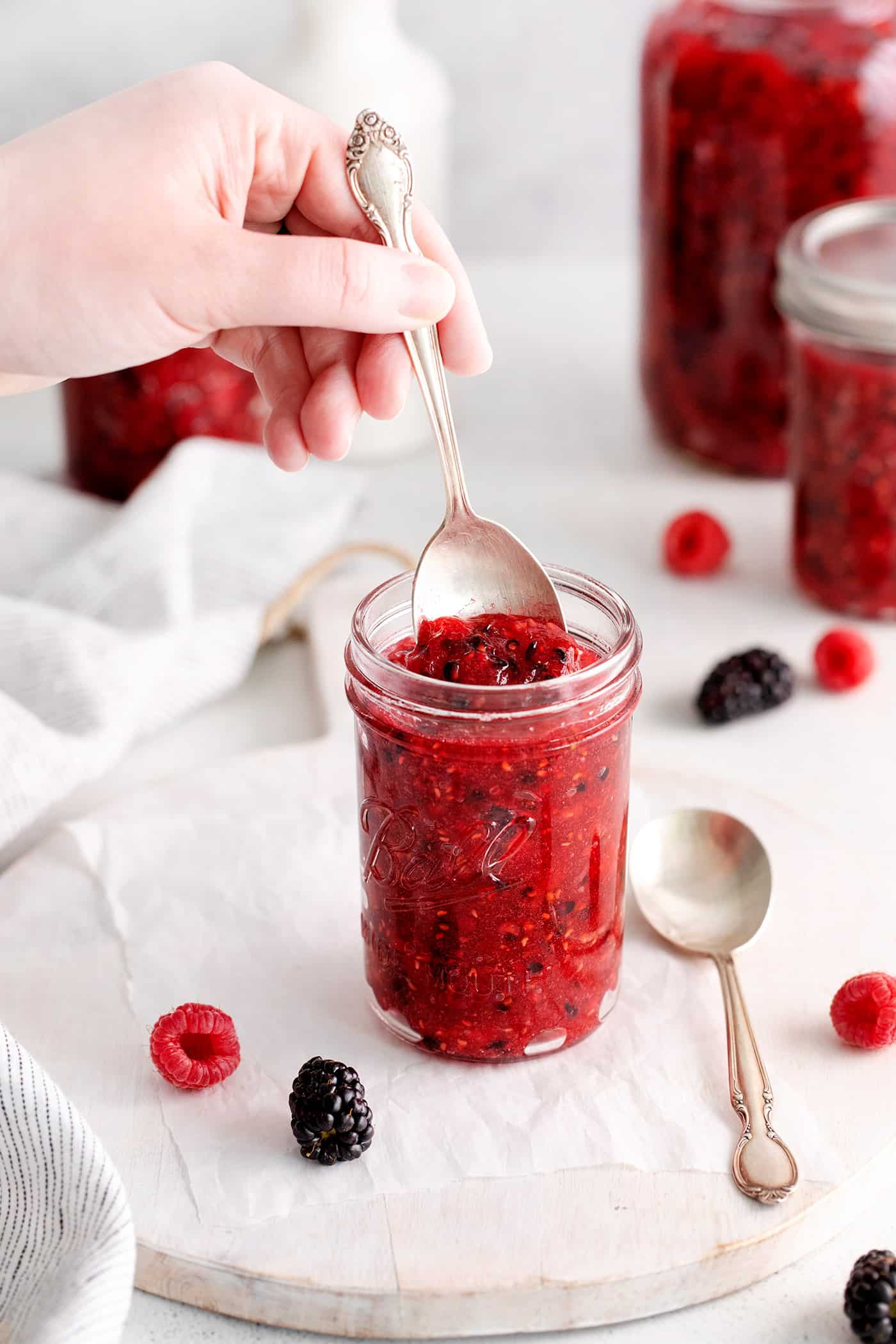 This Raspberry Blackberry Freezer Jam comes together in less than an hour, with just 4 ingredients. No cooking or canning is required! A hand with a spoon in raspberry blackberry freezer jam