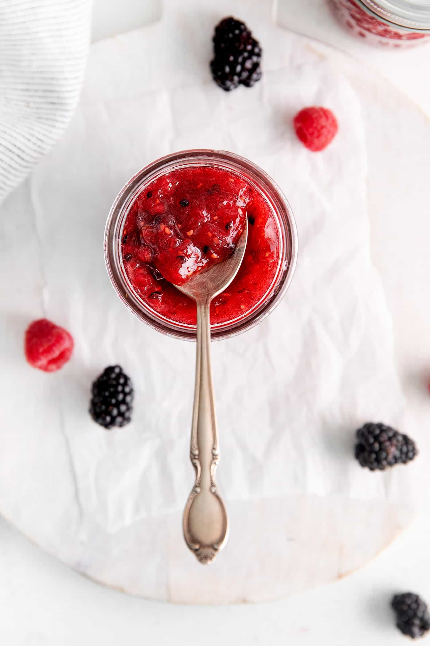 This Raspberry Blackberry Freezer Jam comes together in less than an hour, with just 4 ingredients. No cooking or canning is required! Overhead view of a spoon in a jar of freezer jam