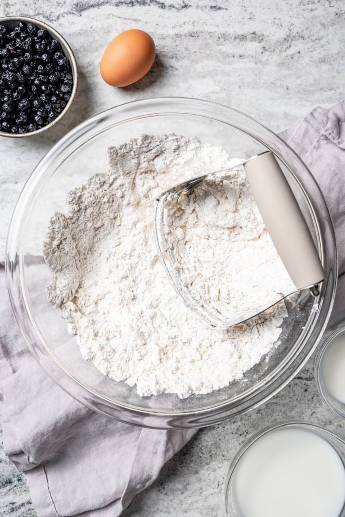 Rich, flaky and dotted with chewy dried blueberries, these blueberry scones are a bakery-style treat you can easily make at home! Overhead view of pastry blender in bowl with dry ingredients and butter