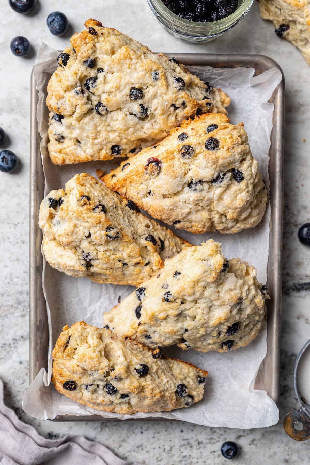 Rich, flaky and dotted with chewy dried blueberries, these blueberry scones are a bakery-style treat you can easily make at home! Overhead view of 5 blueberry scones on parchment lined baking sheet