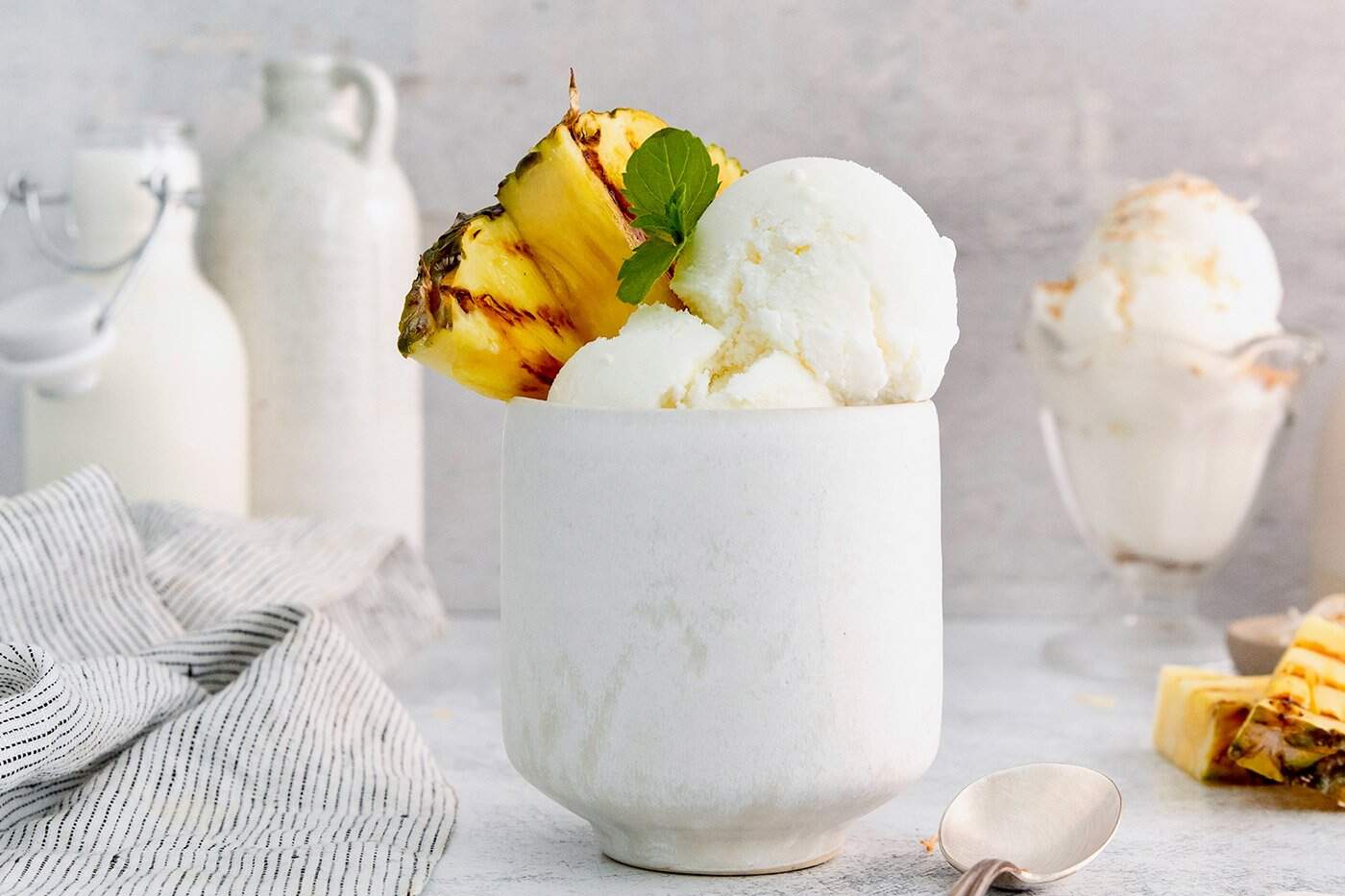Ultra creamy homemade Coconut Ice Cream is pure summertime fun! You only need 3 simple ingredients to whip up this easy recipe. Coconut ice cream in tall bowl with grilled pineapple and sprig of mint