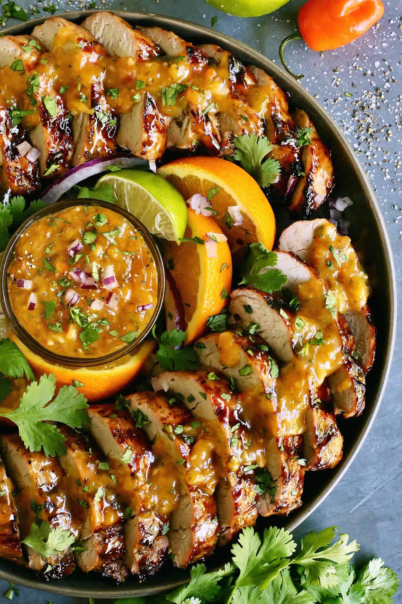 Tender, juicy Grilled Pork Tenderloin is glazed with a sweet peach sauce then topped with an orange-habanero mojo. Overhead view of slices of grilled pork tenderloin