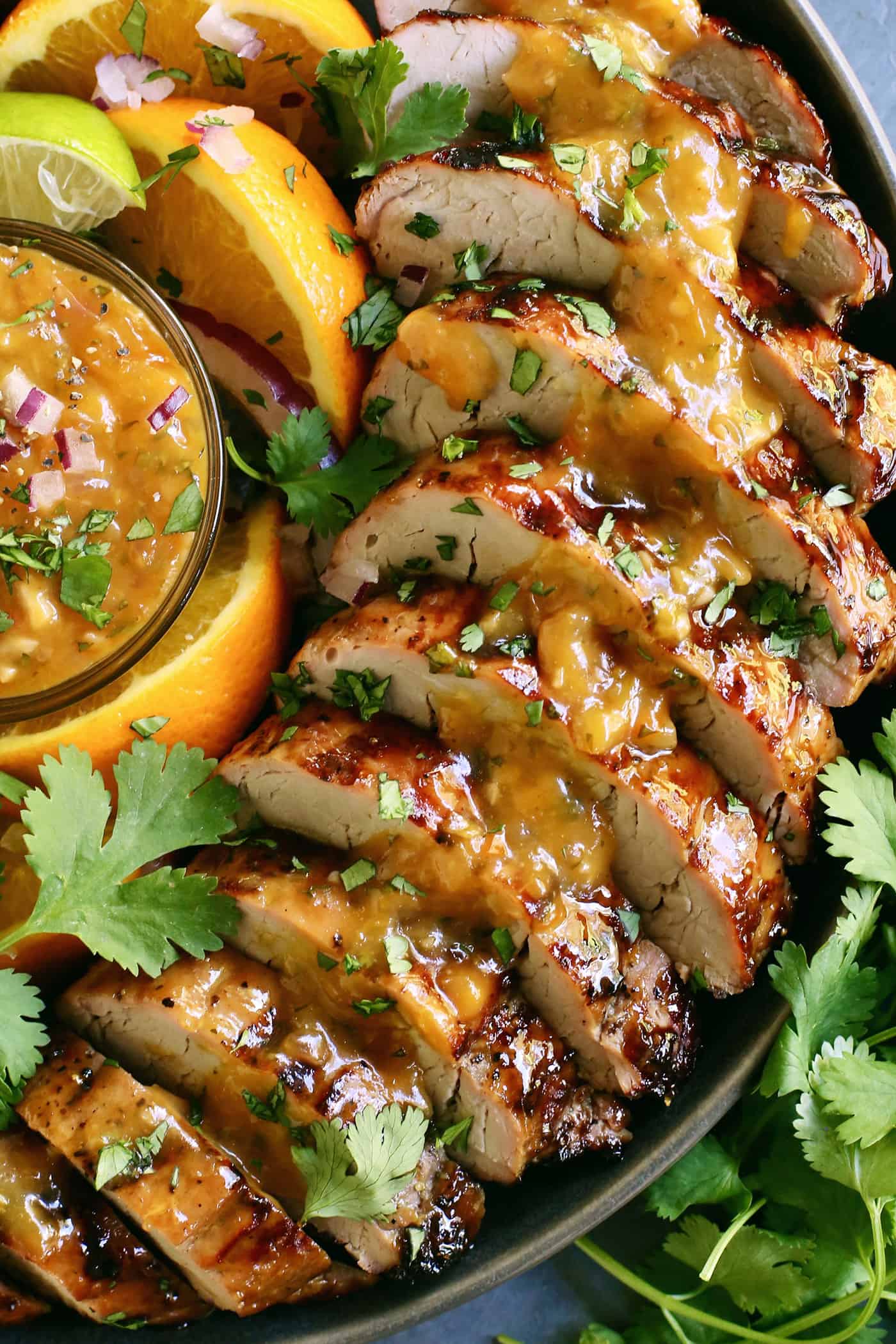 Tender, juicy Grilled Pork Tenderloin is glazed with a sweet peach sauce then topped with an orange-habanero mojo. Close-up of grilled pork tenderloin slices