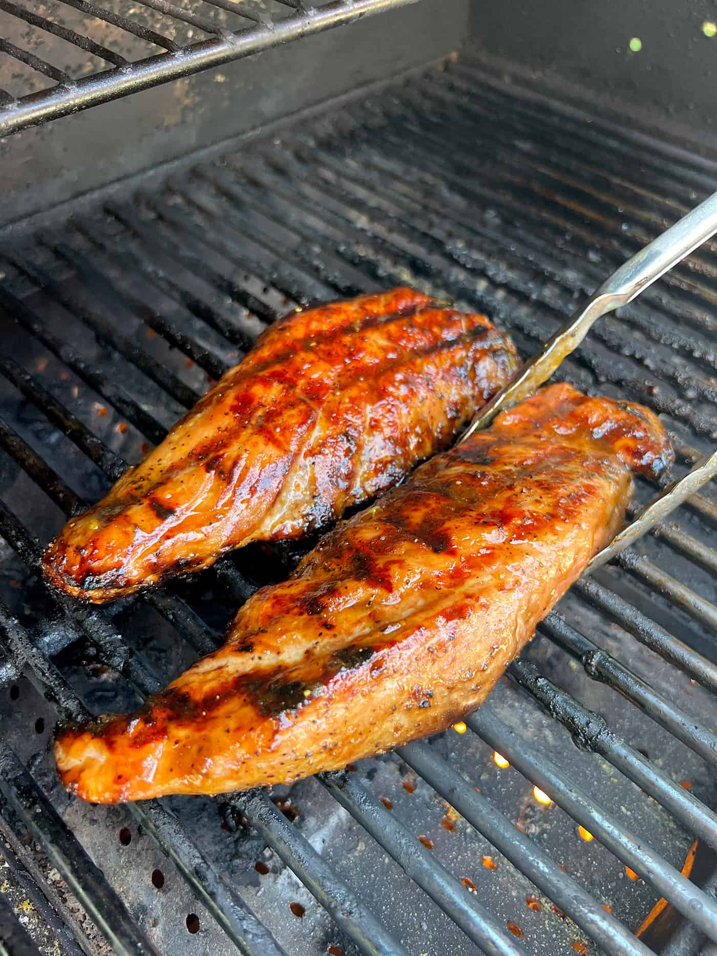 Tender, juicy Grilled Pork Tenderloin is glazed with a sweet peach sauce then topped with an orange-habanero mojo. Tongs removing a pork tenderloin from the grill