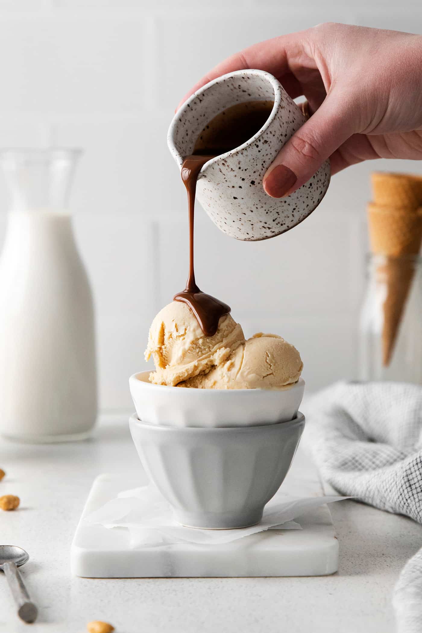 Made with just 5 ingredients and an ice cream maker, this Homemade Peanut Butter Ice Cream is sweet, creamy, and easy to make. A hand pouring hot fudge sauce over peanut butter ice cream