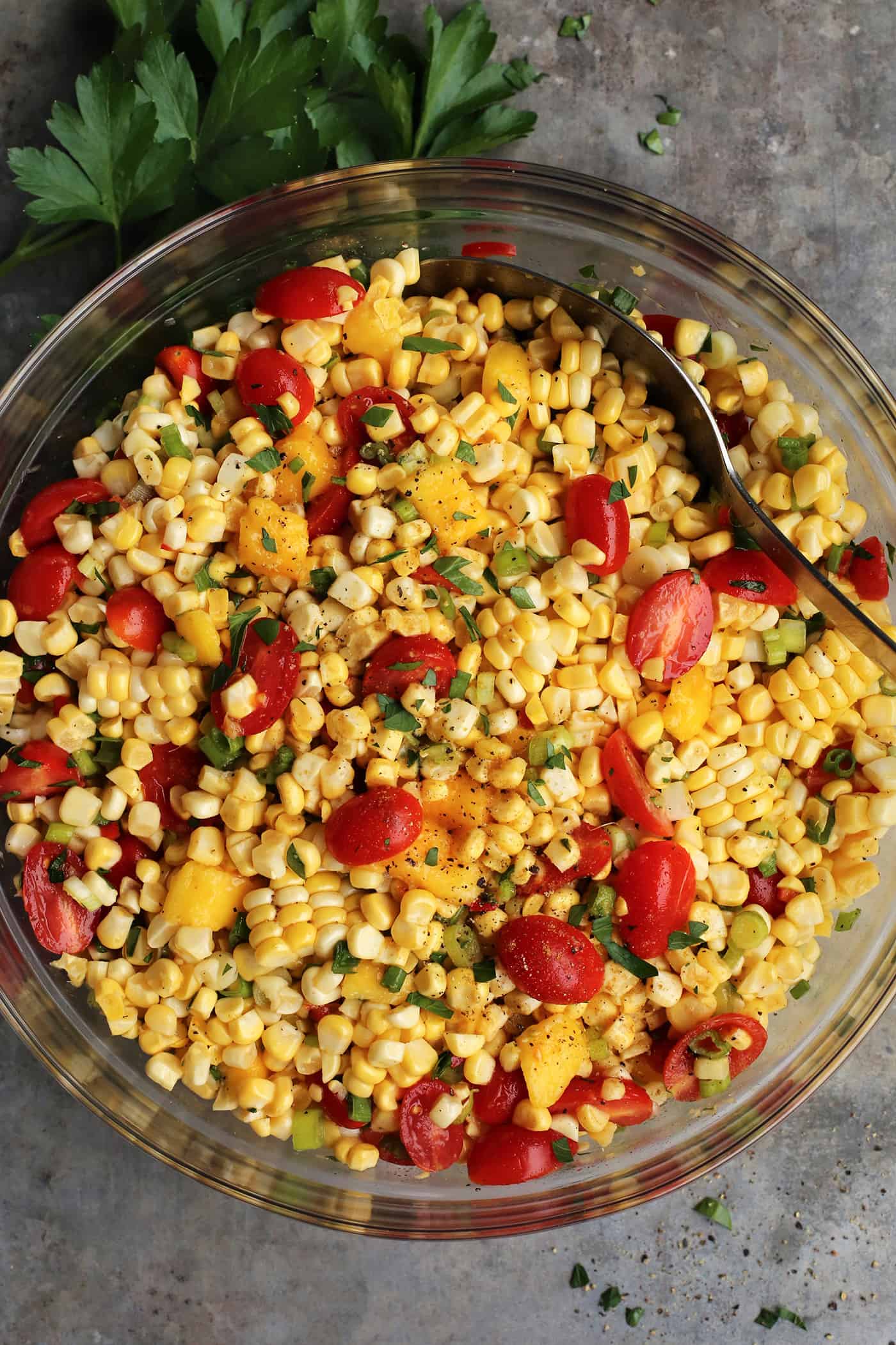 With fresh corn, mangos, tomatoes, and a touch of heat, plus a light and flavorful dressing, this Sweet Corn Salad is a summer treat! Sweet corn salad in a glass bowl with a spoon stirring it