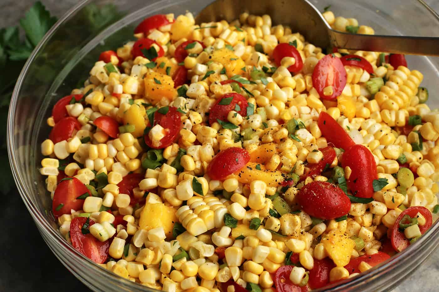 With fresh corn, mangos, tomatoes, and a touch of heat, plus a light and flavorful dressing, this Sweet Corn Salad is a summer treat! A spoon stirring tomato and sweet corn salad