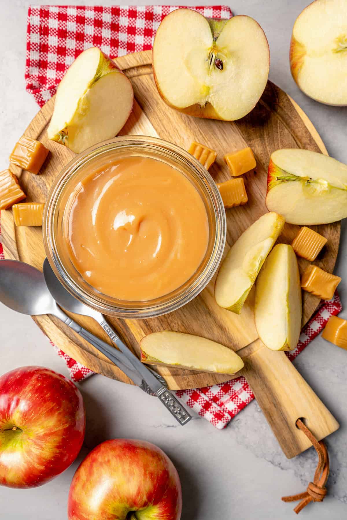 This Caramel Apple Dip beats the pants off of any store-bought caramel dips. Guaranteed! It’s also super easy to make with 3 ingredients. Overhead view of wooden board with jar of caramel apple dip and apple slices