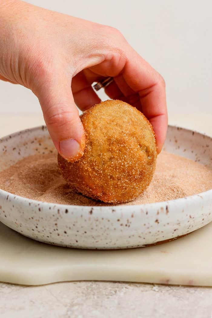 Dipping doughnut muffin into shallow bowl of cinnamon sugar