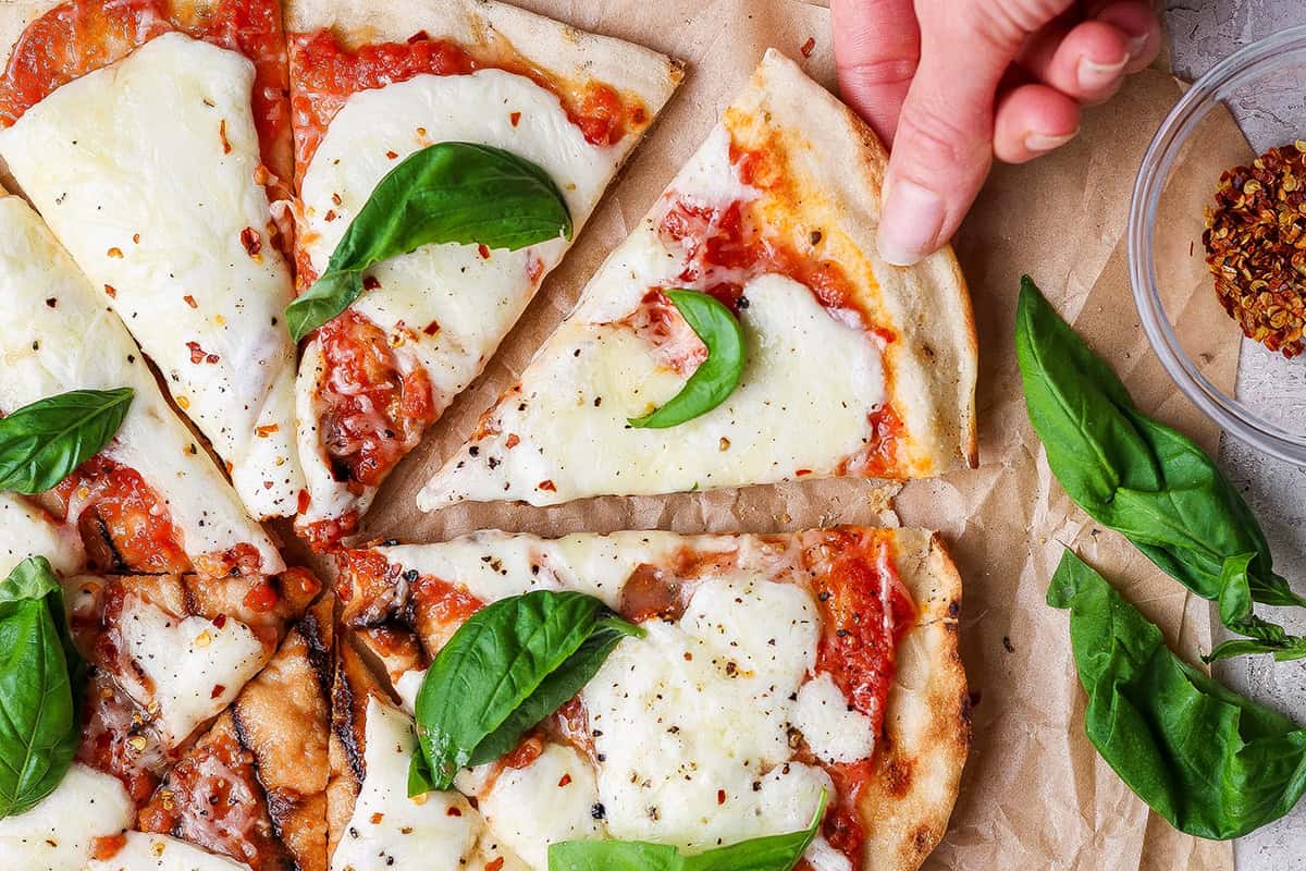 Hand pulling slice of grilled Margherita pizza from pie.