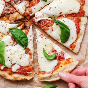 Hand pulling slice of grilled Margherita pizza from pie.
