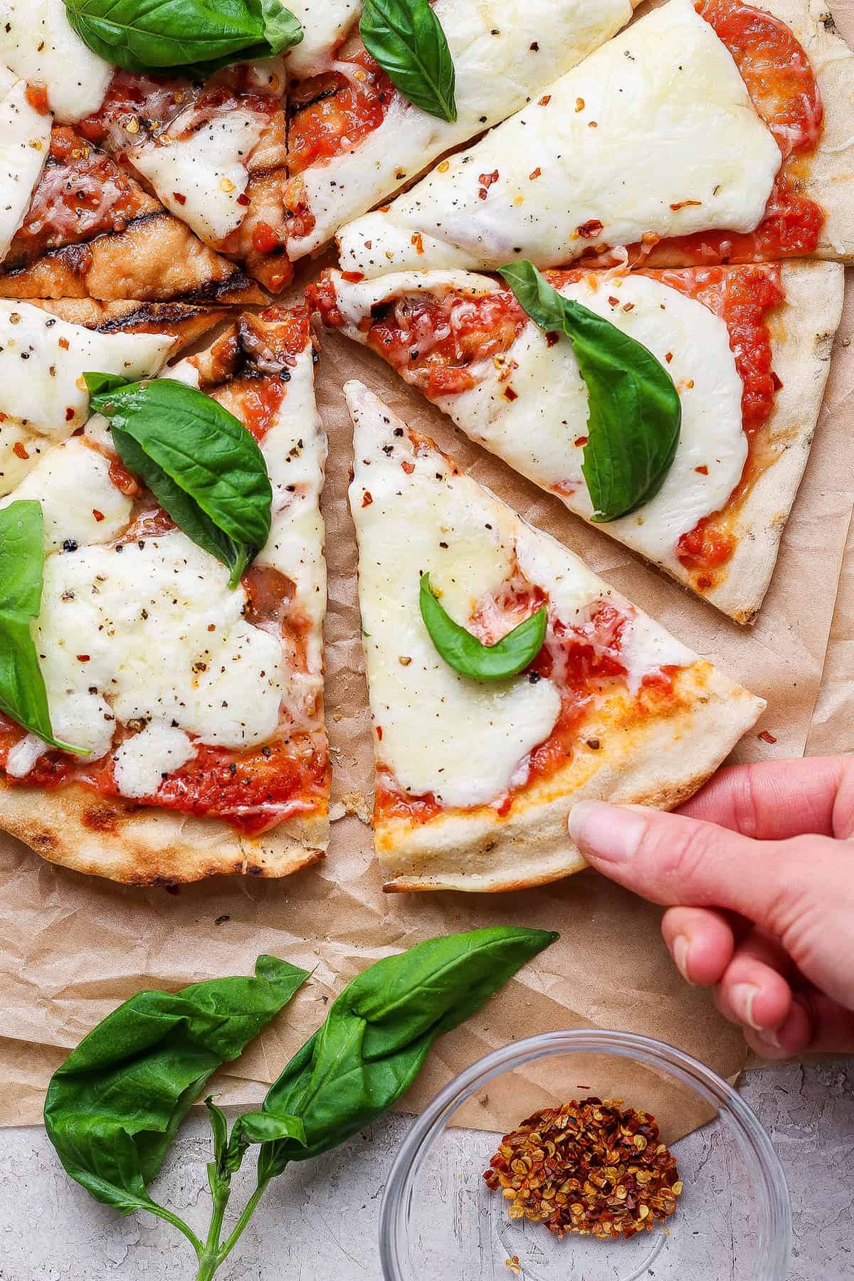 Hand pulling slice of grilled Margherita pizza from pie.