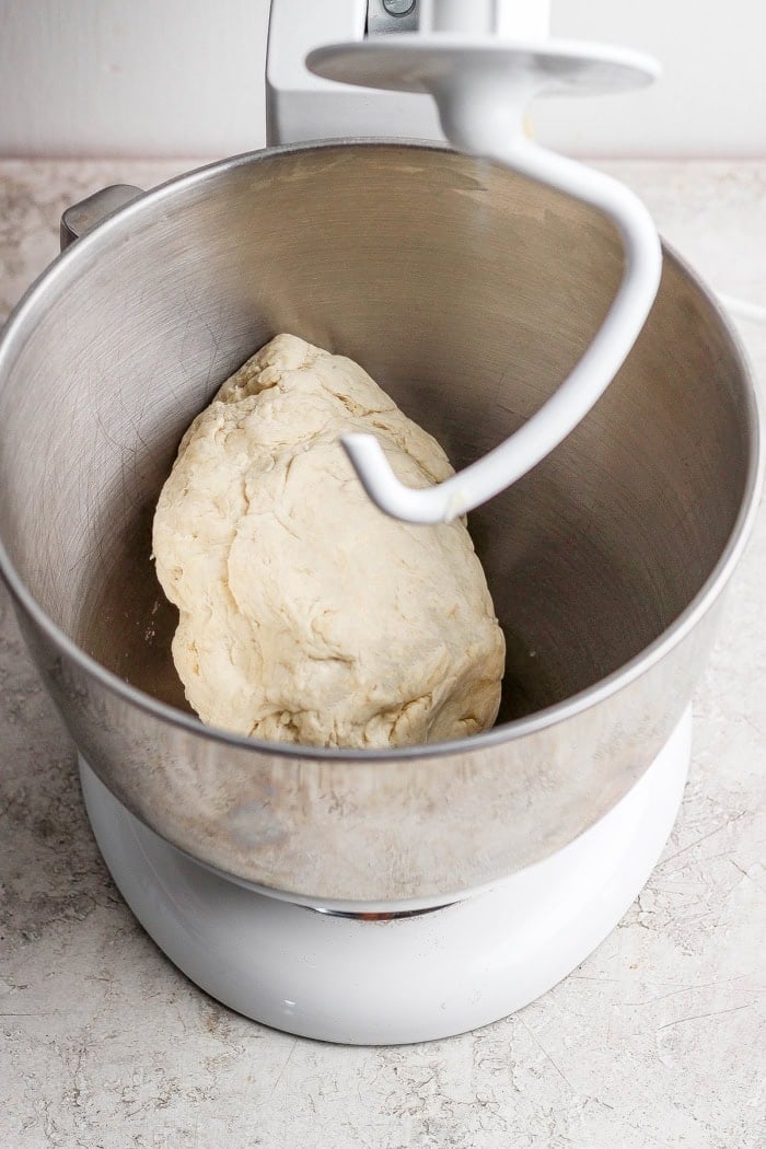 Pizza dough in stand mixer bowl with dough hook.