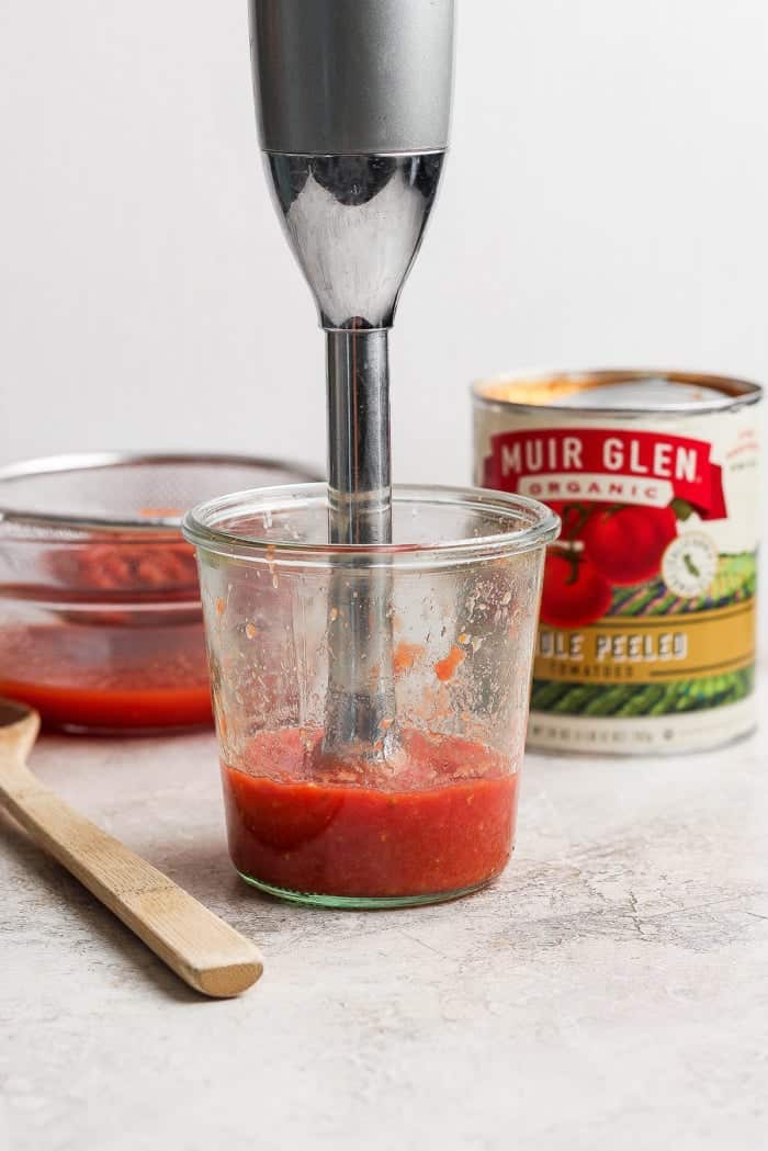 Immersion blender pureeing pizza sauce in jar.