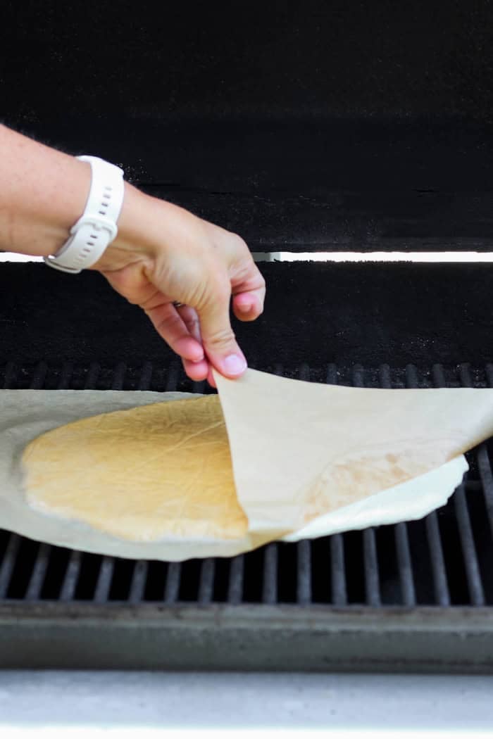 Pulling parchment paper off of dough for grilled pizza crust.