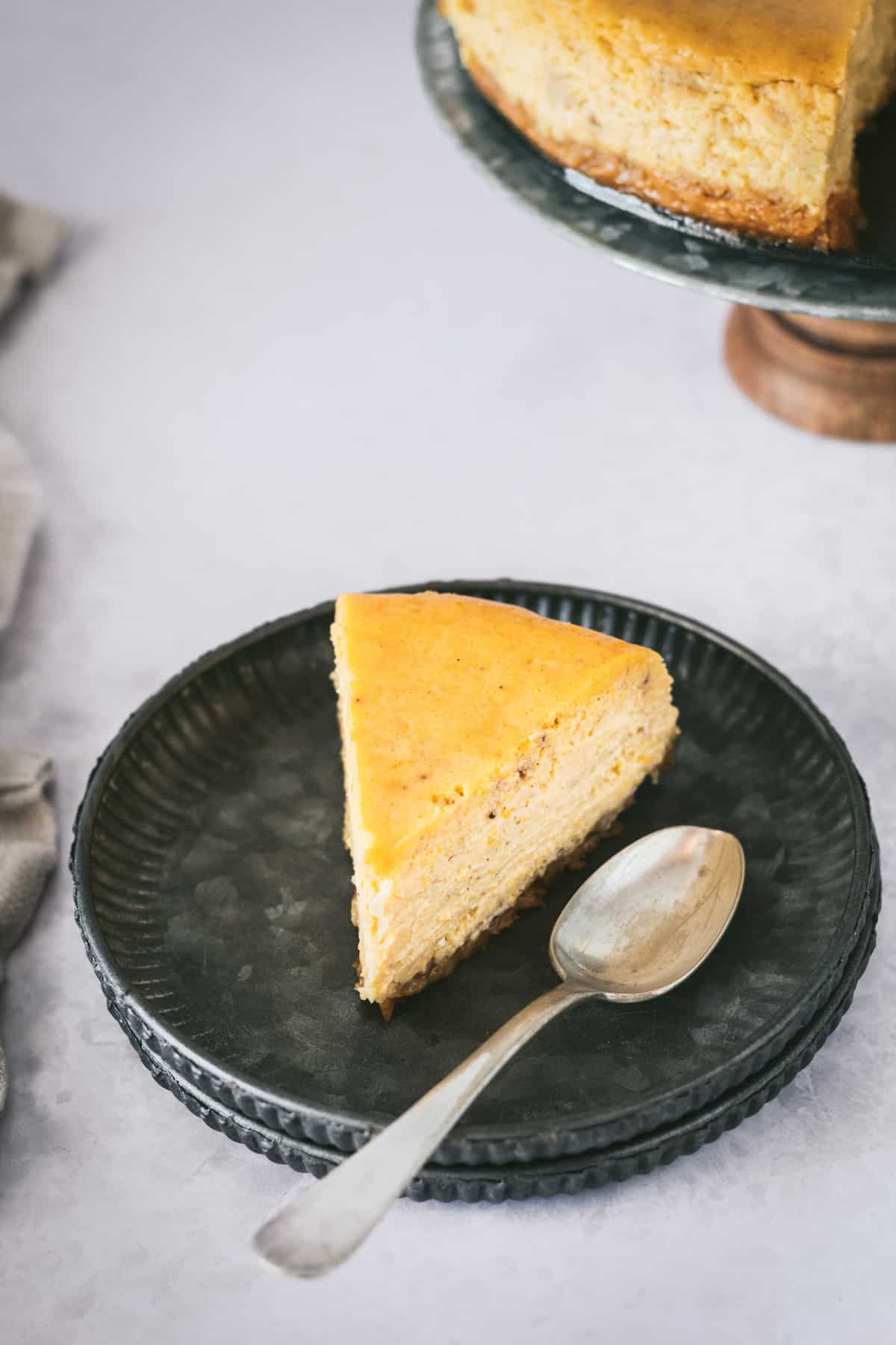 This is the best pumpkin cheesecake recipe! It's creamy, easy to make, and packed with pumpkin flavor, baked in a crunchy gingersnap crust. A slice of pumpkin cheesecake with gingersnap crust on a plate with a spoon