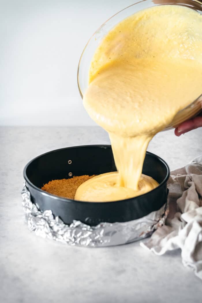This is the best pumpkin cheesecake recipe! It's creamy, easy to make, and packed with pumpkin flavor, baked in a crunchy gingersnap crust. Pumpkin cheesecake batter being poured into a springform pan.