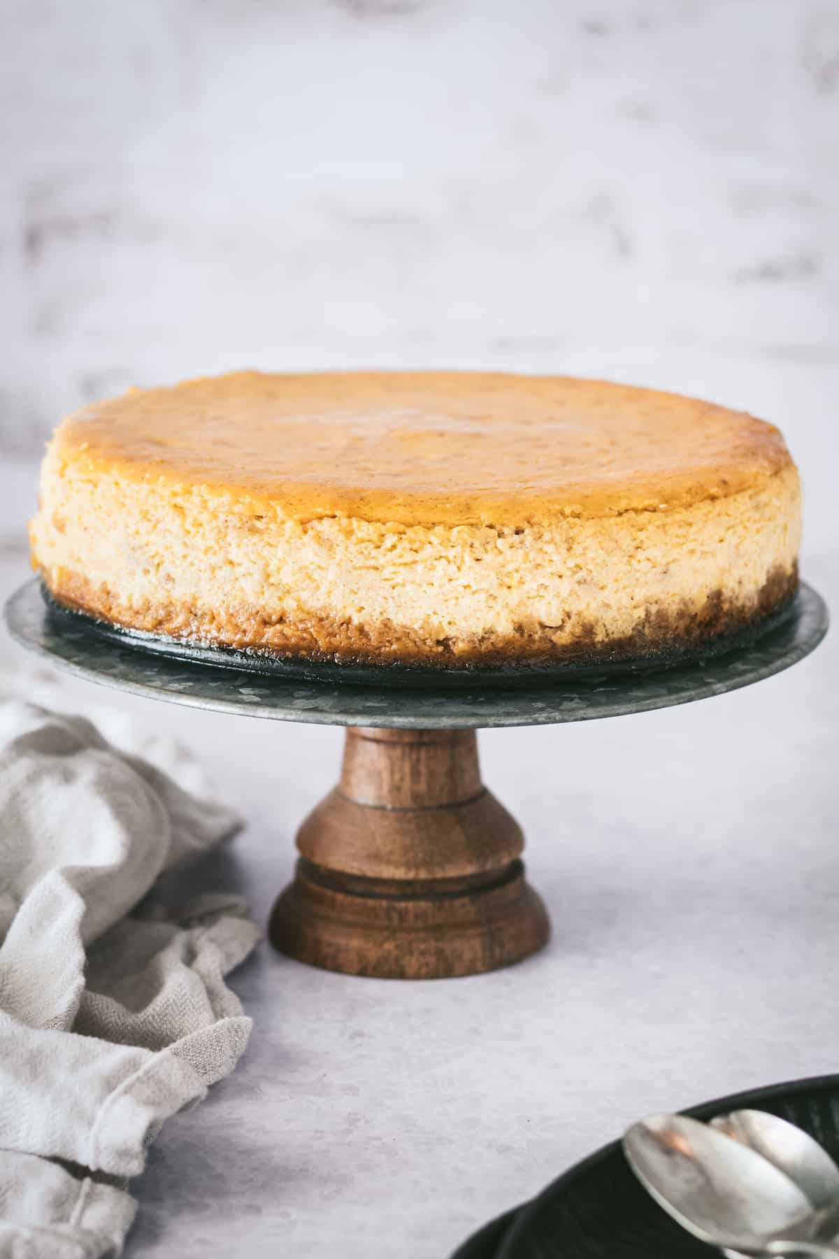 This is the best pumpkin cheesecake recipe! It's creamy, easy to make, and packed with pumpkin flavor, baked in a crunchy gingersnap crust. Creamy pumpkin cheesecake with gingersnap crust on a serving stand