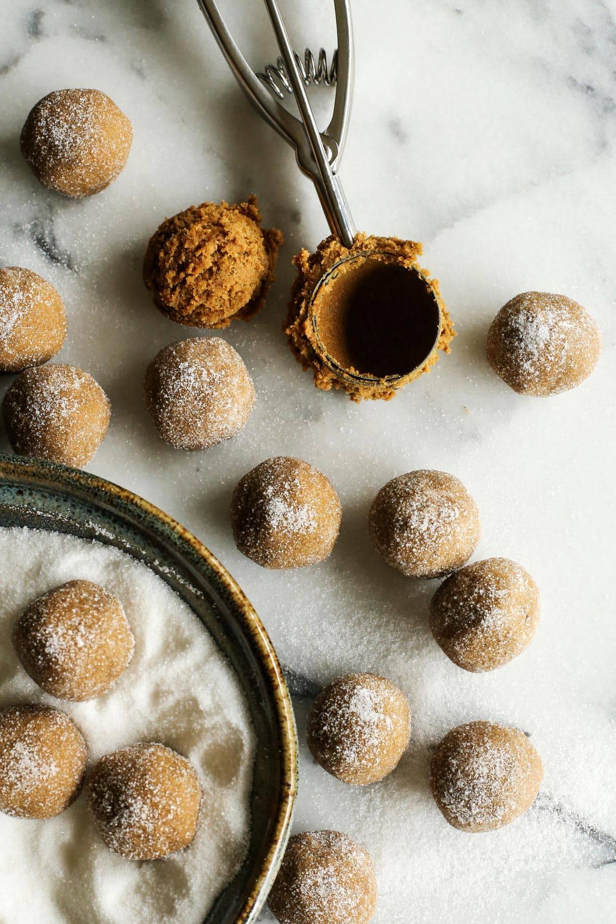 This Ginger Molasses Cookies recipe is easy to make, with no need to chill the dough, and creates perfectly soft and chewy cookies. A cookie scoop and balls of cookie dough rolled in sugar.