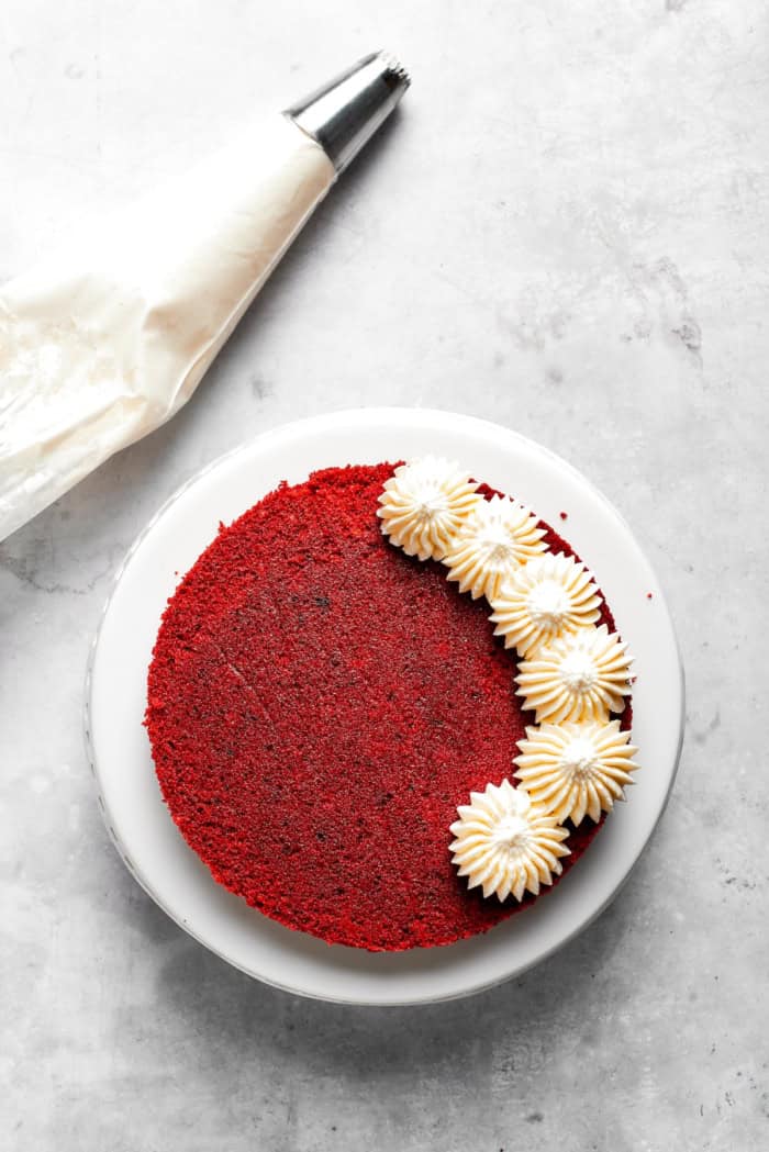 Overhead view of frosting partially piped onto top of red velvet cake