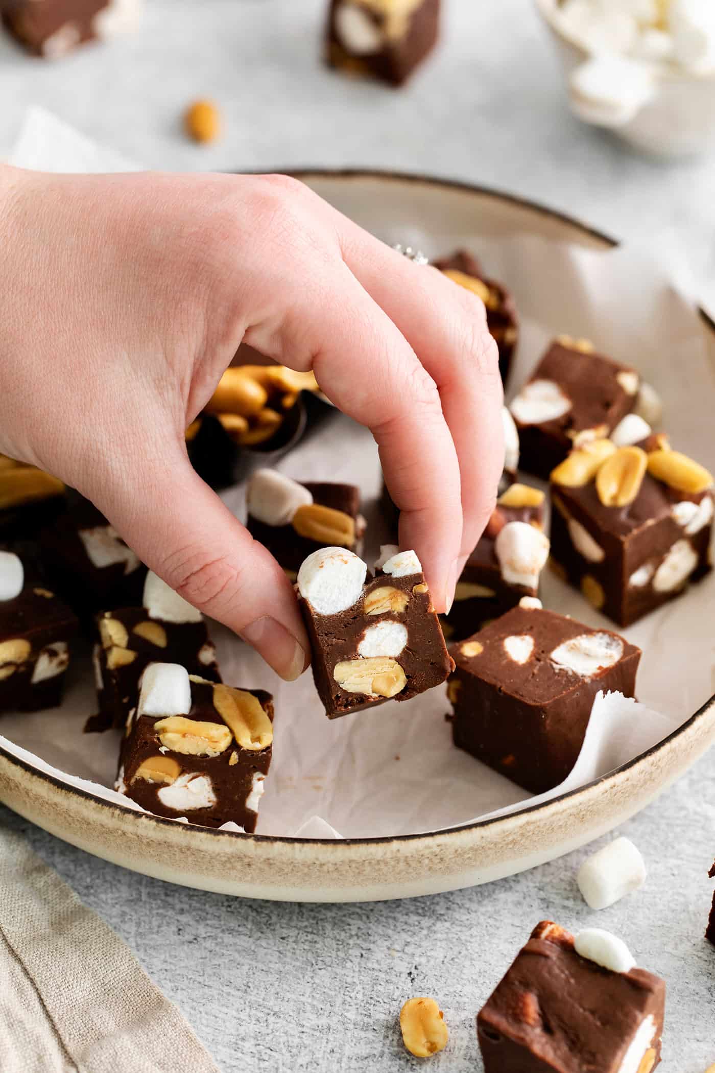 Quick and easy, this Rocky Road Fudge is made with creamy chocolate fudge stuffed with salty, crunchy peanuts and sweet, soft marshmallows. A hand grabbing a piece of rocky road fudge