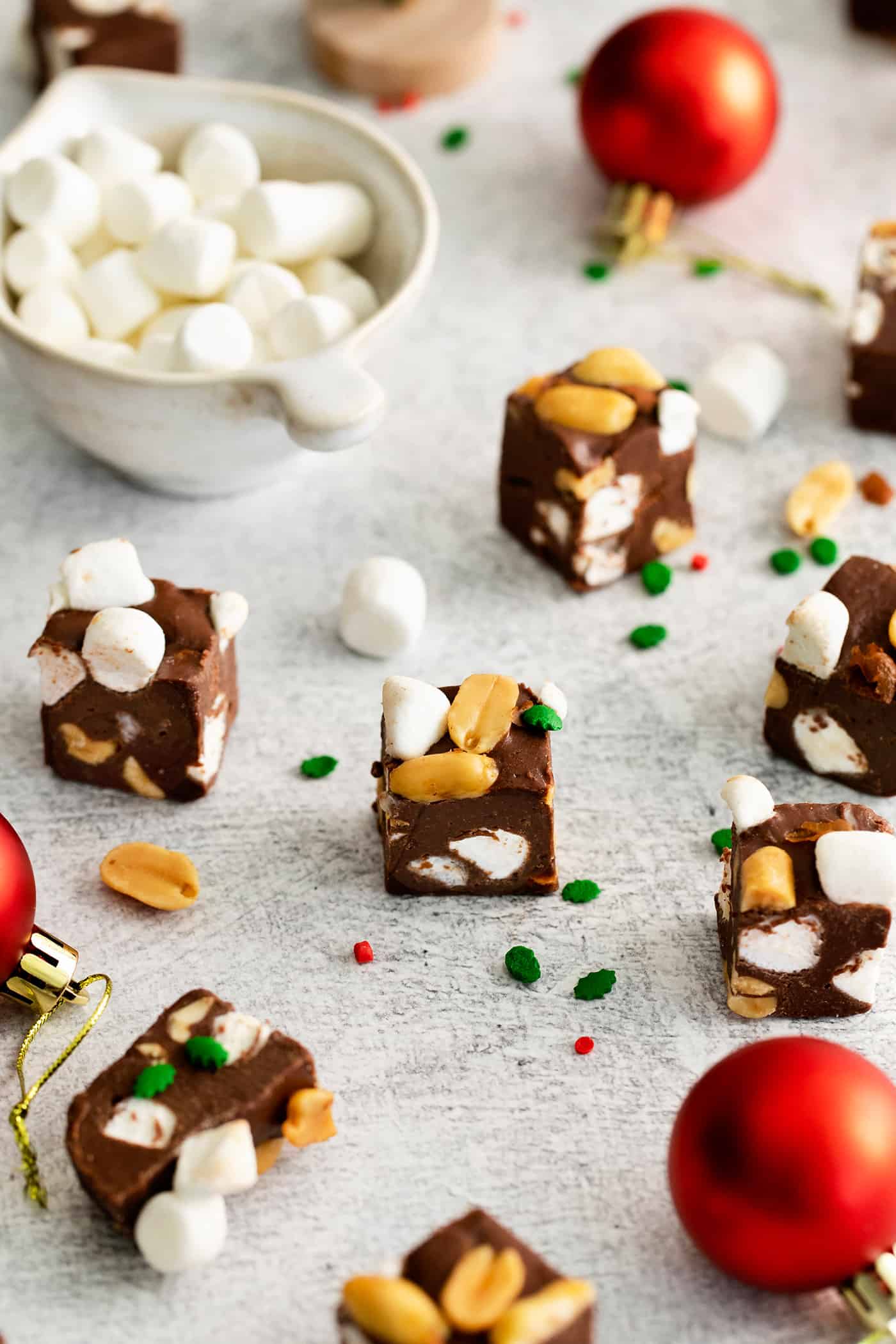 Quick and easy, this Rocky Road Fudge is made with creamy chocolate fudge stuffed with salty, crunchy peanuts and sweet, soft marshmallows. Rocky road fudge on the table with Christmas bulbs