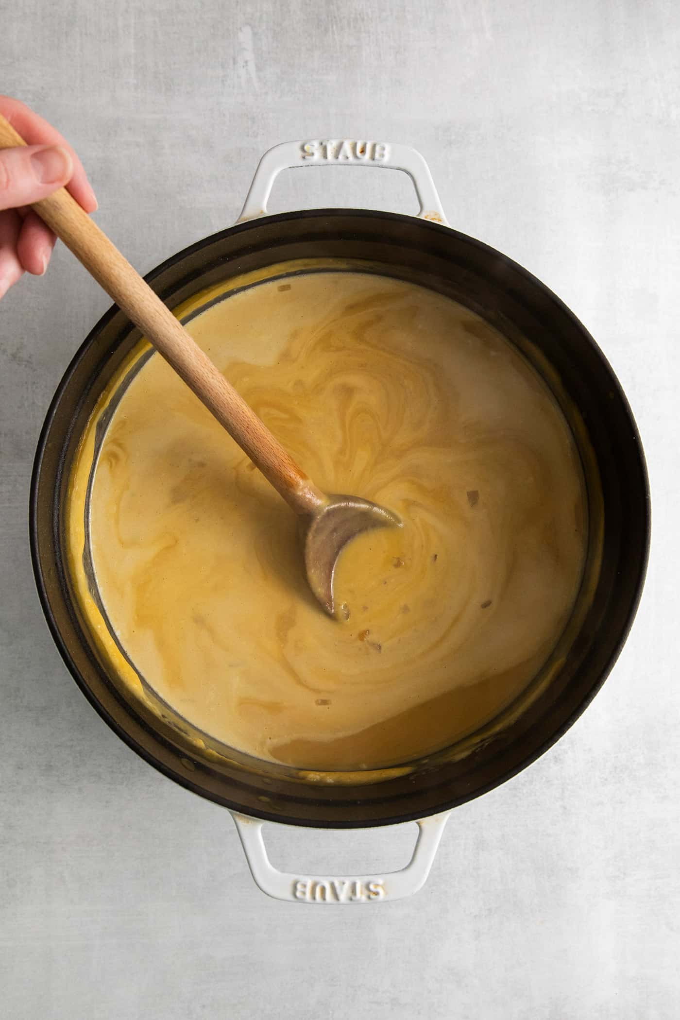 This Creamy Squash Soup with Cranberry Relish is made with squash, cream, warm spices and finished with a tart cranberry topping. A wooden spoon stirring cream into squash soup