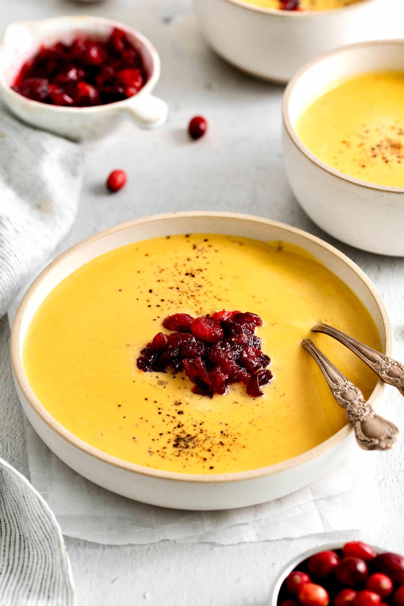 This Creamy Squash Soup with Cranberry Relish is made with squash, cream, warm spices and finished with a tart cranberry topping. Angled view of a bowl of squash soup with cranberry relish