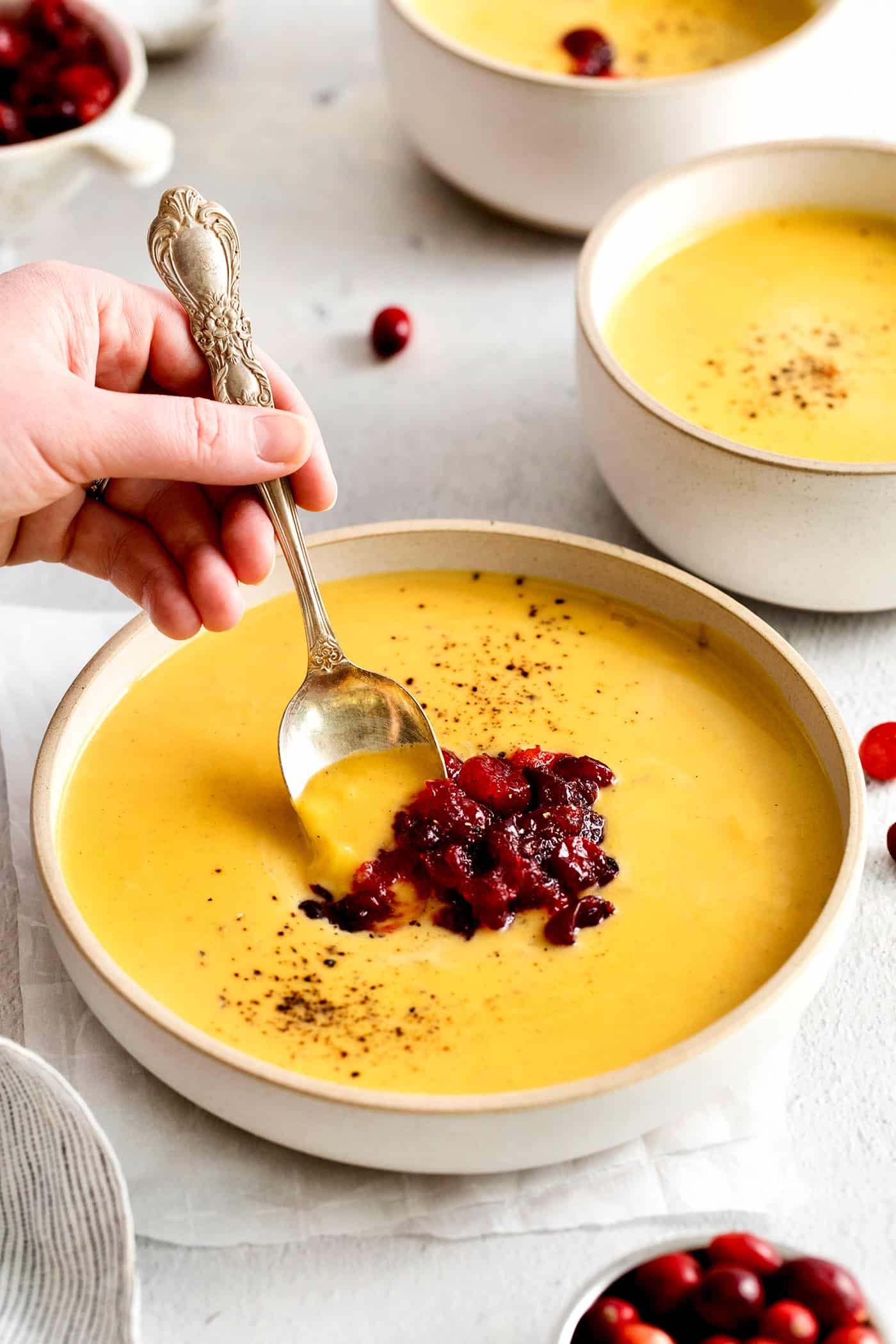 This Creamy Squash Soup with Cranberry Relish is made with squash, cream, warm spices and finished with a tart cranberry topping. A spoon in a bowl of squash soup