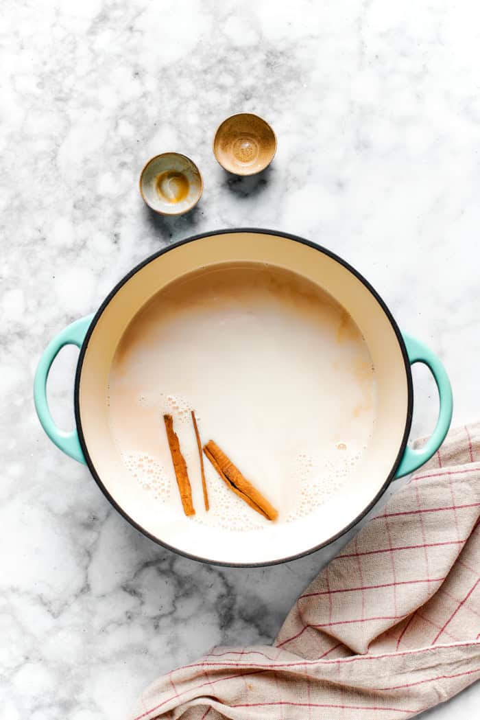 This vanilla steamer recipe combines warm milk with cinnamon, vanilla and almond extract for a cozy drink to savor all winter long. Overhead view of cinnamon sticks in pan of warm milk