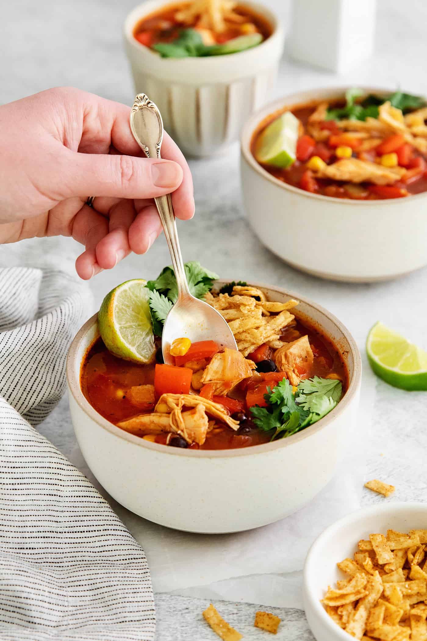 This easy chicken tortilla soup recipe is loaded with Mexican-style flavor, ready in 40 minutes! A perfect one pot soup recipe for weeknights! A hand holding a spoon in a bowl of chicken tortilla soup
