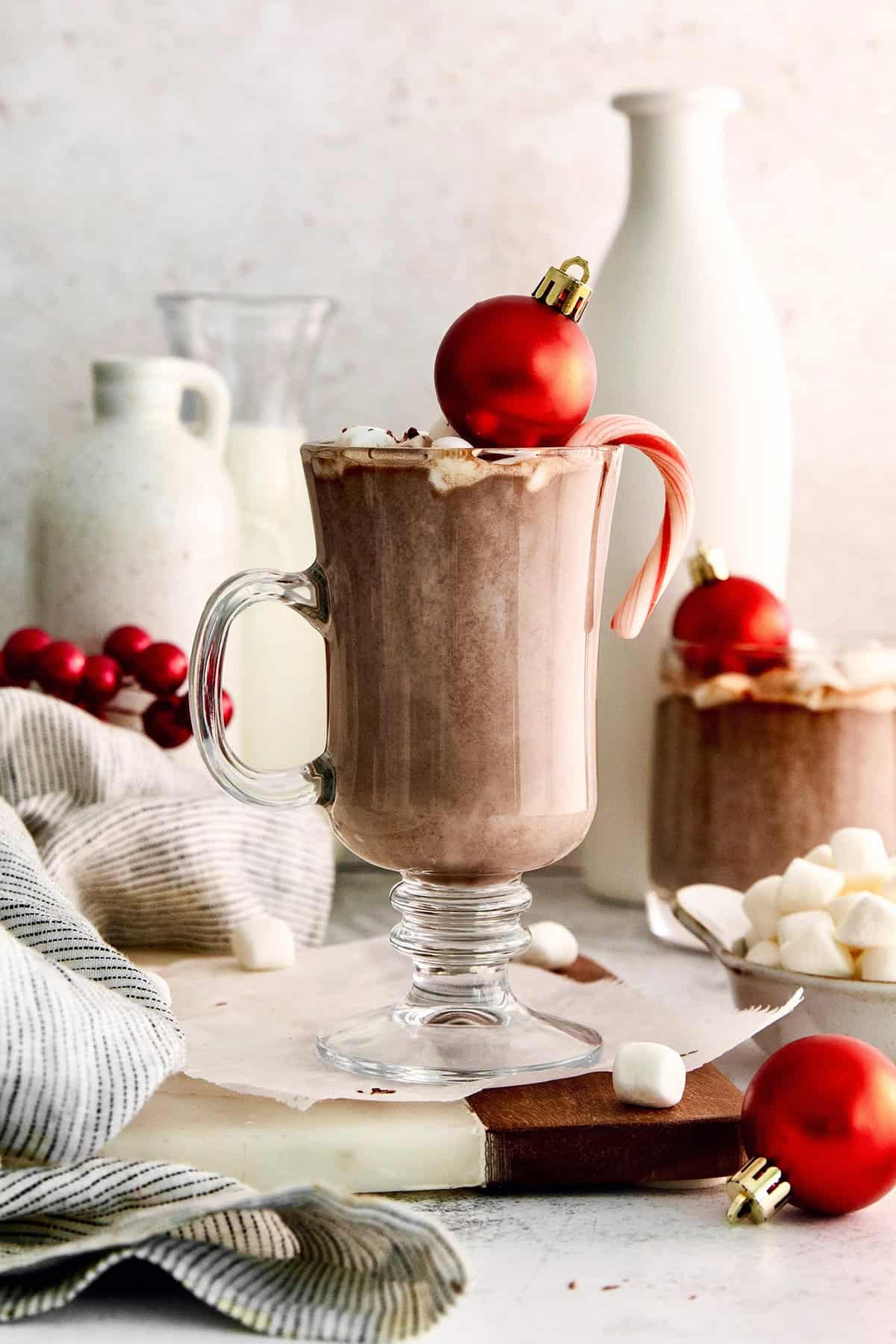 This recipe for homemade hot chocolate makes the creamiest and most decadent hot cocoa ever! It's easy to make and impossible to resist. Hot chocolate in glass mug with marshmallows, candy cane, and ornament for garnish
