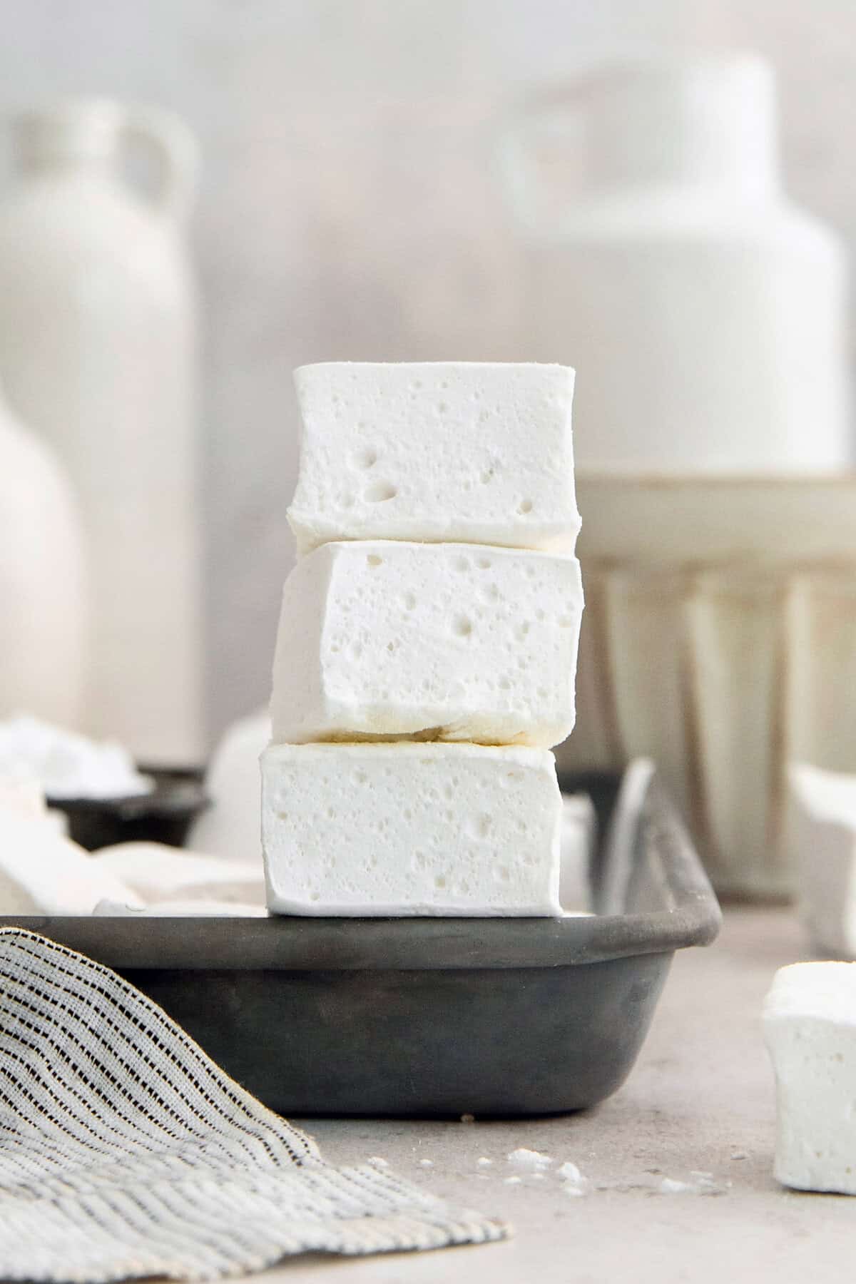 Homemade marshmallows are easier than you think! This recipe yields perfect fluffy marshmallows that are SO much better than store-bought. Stack of 3 homemade marshmallows on edge of sheet pan