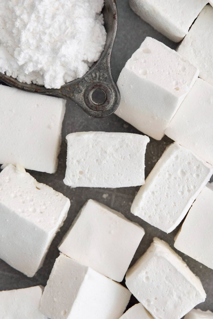Homemade marshmallows are easier than you think! This recipe yields perfect fluffy marshmallows that are SO much better than store-bought. Overhead view of homemade marshmallows and powdered sugar in cup