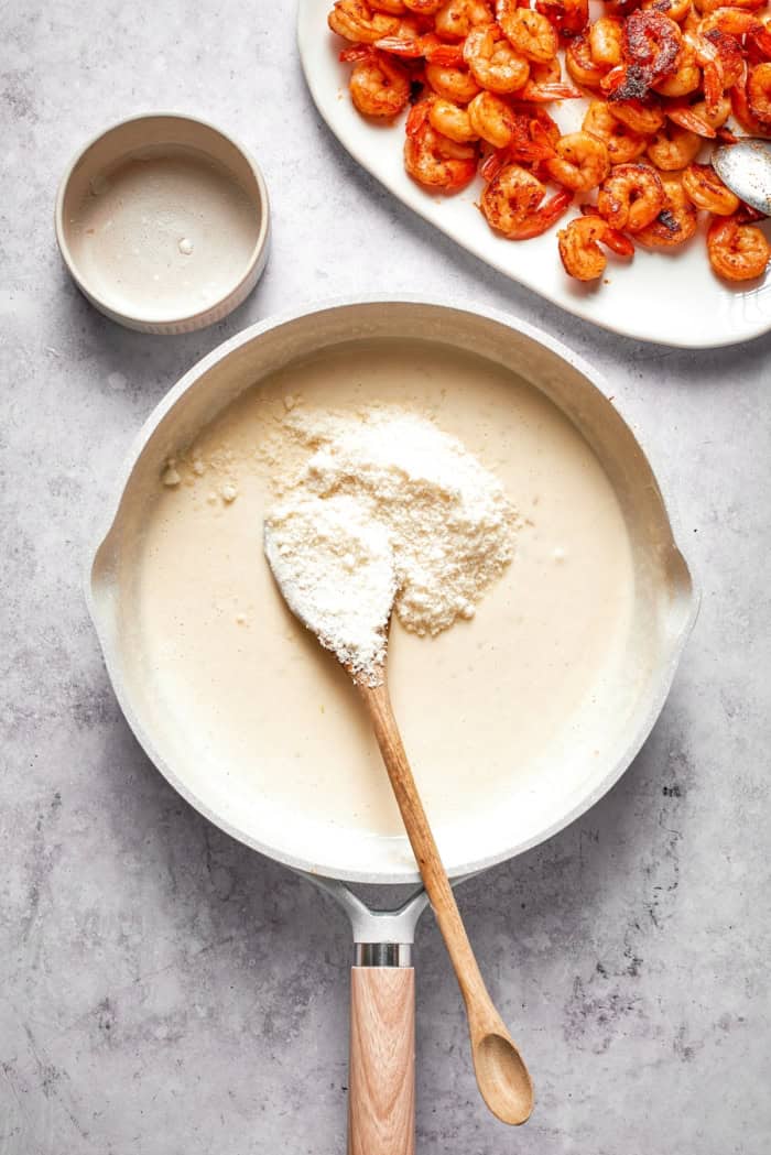 Rich without being heavy, garlicky with just a bit of heat, this Creamy Shrimp Pasta is a restaurant-worthy meal ideal for a date-night-in! Parmesan cheese added to cream sauce in skillet.