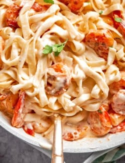 Creamy shrimp pasta in skillet with serving spoon.