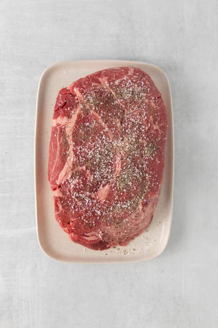Made with chuck roast, potatoes, carrots, and onions in a beef broth, this Classic Pot Roast is comfort food at its finest. Hearty & filling! Beef chuck roast seasoned with salt and pepper on a white plate