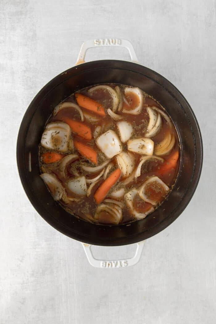 Made with chuck roast, potatoes, carrots, and onions in a beef broth, this Classic Pot Roast is comfort food at its finest. Hearty & filling! Overhead view of veggies and chuck roast in a pot with beef broth