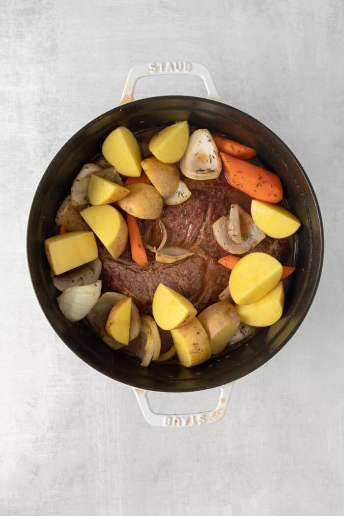 Made with chuck roast, potatoes, carrots, and onions in a beef broth, this Classic Pot Roast is comfort food at its finest. Hearty & filling! Potatoes on top of a chuck roast in a pot
