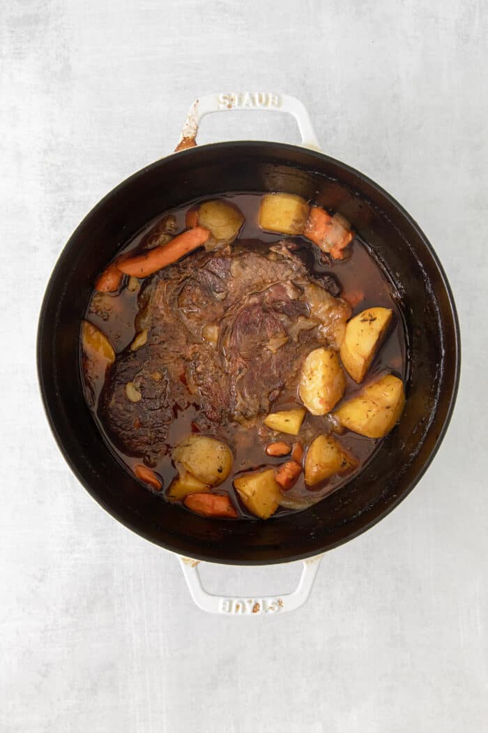 Made with chuck roast, potatoes, carrots, and onions in a beef broth, this Classic Pot Roast is comfort food at its finest. Hearty & filling! Overhead view of a pot roast and vegetables in a pot