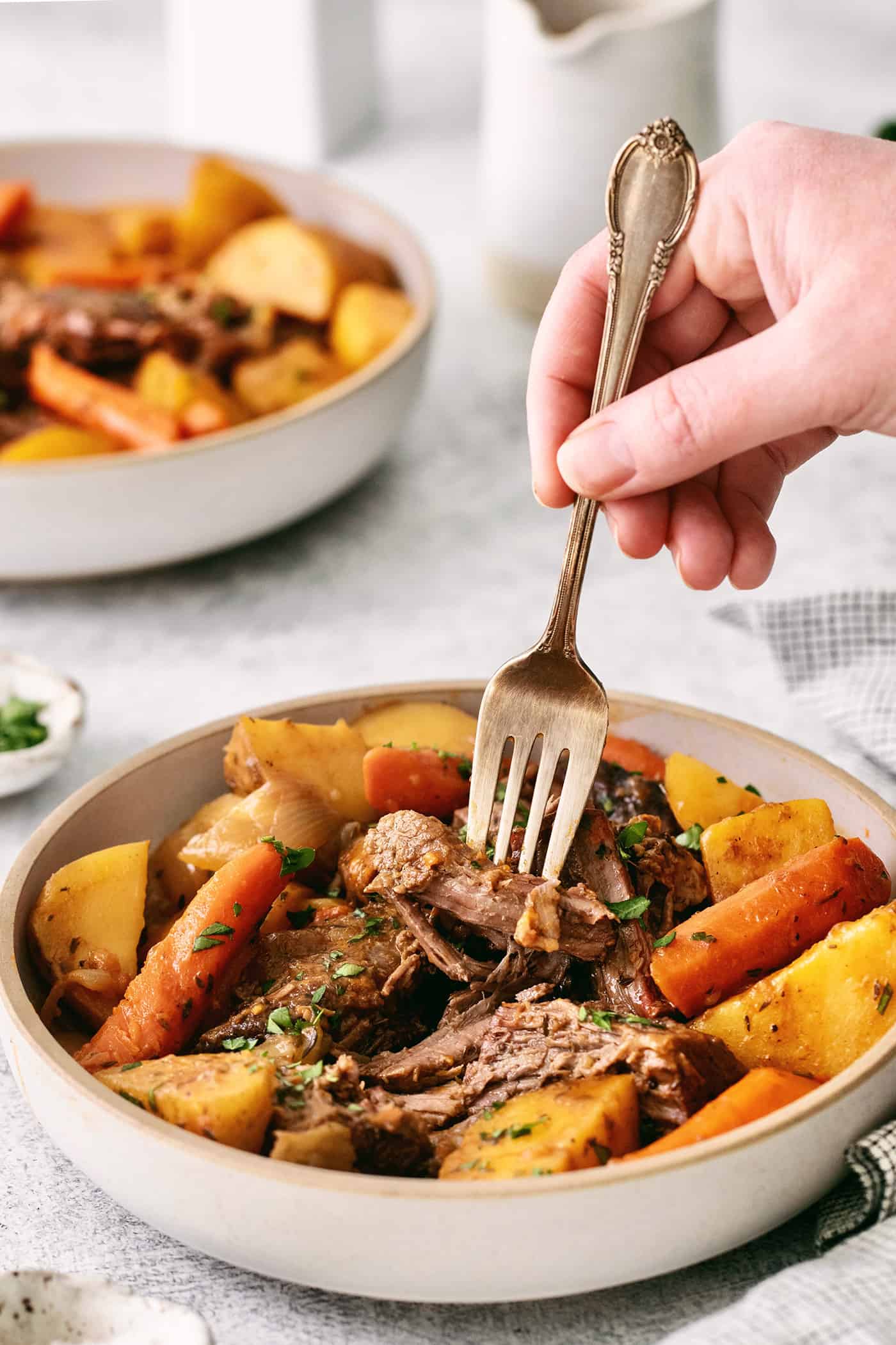 Made with chuck roast, potatoes, carrots, and onions in a beef broth, this Classic Pot Roast is comfort food at its finest. Hearty & filling! A fork diving into a piece of pot roast in a bowl