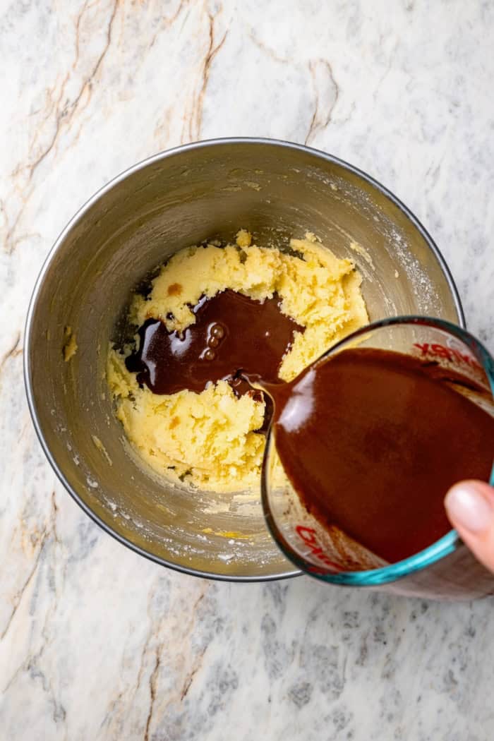 This classic German Chocolate Cake recipe is a moist, rich three-layer chocolate cake topped with a nutty coconut-pecan frosting. Perfection! Pouring melted chocolate and water into creamed butter and sugar