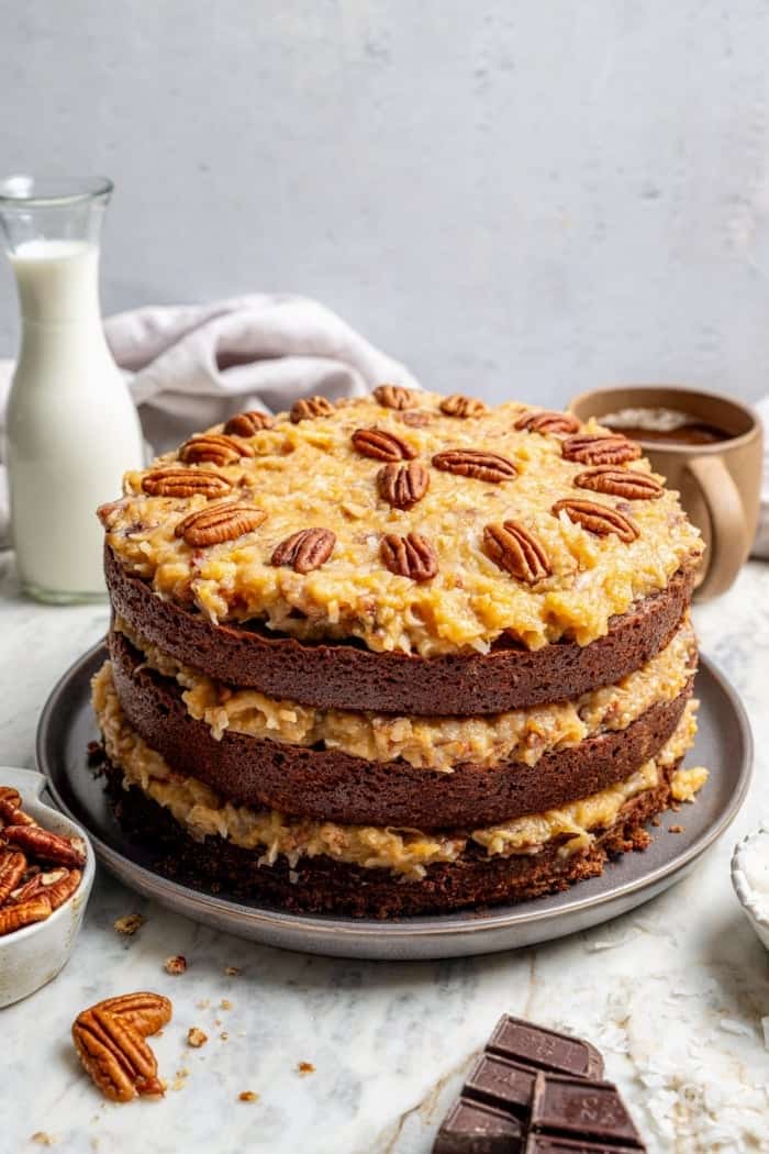 This classic German Chocolate Cake recipe is a moist, rich three-layer chocolate cake topped with a nutty coconut-pecan frosting. Perfection! Whole German chocolate cake on platter