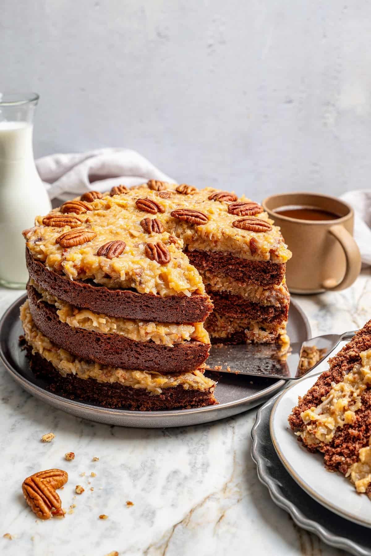 This classic German Chocolate Cake recipe is a moist, rich three-layer chocolate cake topped with a nutty coconut-pecan frosting. Perfection! German chocolate cake on platter with one slice removed to show layers