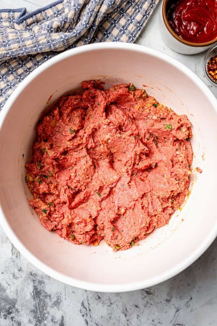 Spicy Meatloaf is a classic with a kick! It has a little Tex-Mex flair thanks to cumin and jalapeño, with a chili glaze to bring the heat. Ground beef meatloaf mixture in mixing bowl.