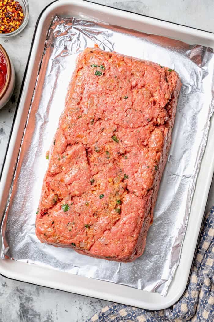 Spicy Meatloaf is a classic with a kick! It has a little Tex-Mex flair thanks to cumin and jalapeño, with a chili glaze to bring the heat. Ground beef mixture shaped into loaf on pan.